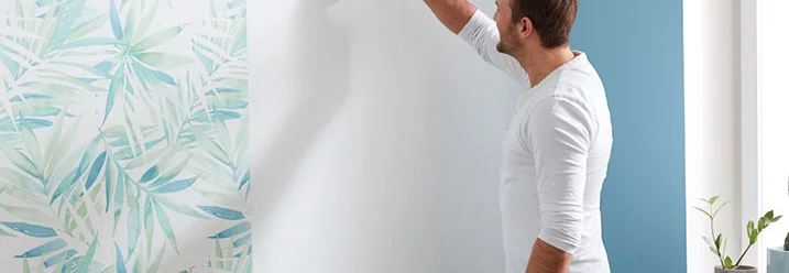 Person bringt mit einer Bürste Kleister an eine Wand an